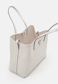 Sac cabas blanc perforé avec des bretelles fines, présentant une surface texturée, une forme structurée et des accents de quincaillerie dorée.