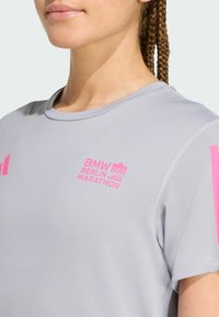 Camiseta atlética gris con acentos rosas y el logo "BMW BERLIN MARATHON". Fabricada con material transpirable, tiene mangas cortas y un diseño de cuello redondo.