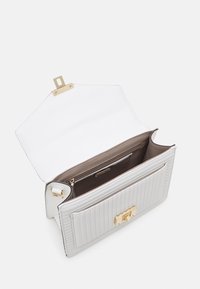 Hvid quiltet læderhåndtaske med guldbeslag. Indvendigt med brun foring og en lynlåslomme. Åben klapdesign for nem adgang.