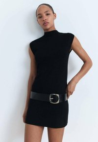 Robe noire sans manches avec un col montant et une silhouette ajustée, dotée d'une large ceinture noire avec une boucle carrée en argent.