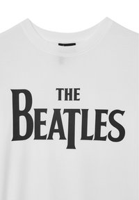 T-shirt bianco in cotone con la scritta audace "THE BEATLES" in un carattere serif stilizzato, col tradizionale scollo a crew e una consistenza morbida.