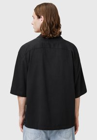 Camicia a maniche corte nera in cotone, con colletto classico, vestibilità rilassata e taglio dritto con una leggera fessura laterale all'orlo.