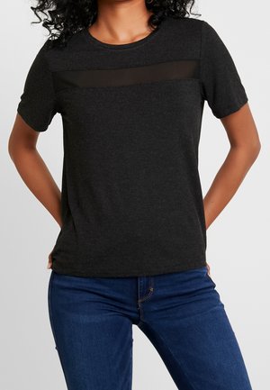 Zwart T-shirt met korte mouwen en een doorschijnend mesh paneel over de borst, gemaakt van een zachte stof met een gladde textuur, gecombineerd met een blauwe spijkerbroek.