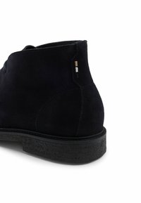 Stivale alla caviglia in suede nero con superficie testurizzata, forma arrotondata e suola in gomma. Presenta un sottile accento multicolore vicino al tallone.