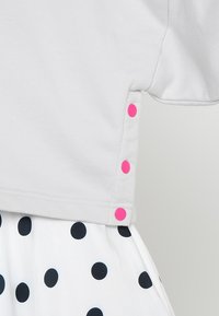 Maglietta grigia con maniche corte e bottoni automatici rosa lungo il lato. Abbinata a una gonna bianca decorata con grandi pois neri.