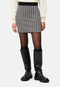 Schwarz-weiß gemusterter Minirock mit einem elastischen schwarzen Bund, kombiniert mit knielangen schwarzen Lederstiefeln und schwarzen gerippten Socken.