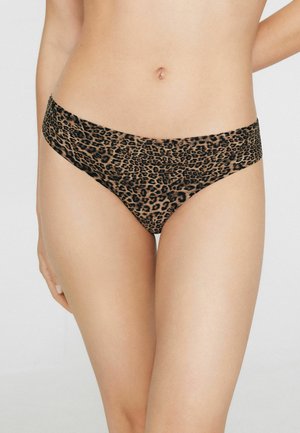 Mujer con ropa interior estilo hipster de estampado de leopardo, mostrando el abdomen y la parte superior de las piernas sobre un fondo liso.