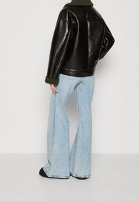 Veste en cuir noir avec un col texturé vert, associée à un jean flare bleu clair. La veste présente une coupe carrée et un ajustement décontracté.