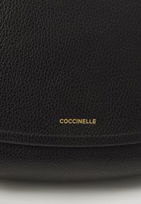 Borsa a spalla in pelle nera con finitura testurizzata. Logo dorato "Coccinelle" nella parte inferiore. Design elegante con forma arrotondata.