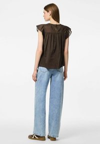 Blusa marrone a maniche corte con dettagli a volant e chiusura a bottone sul retro, abbinata a jeans in denim leggeri a gamba larga di colore azzurro.