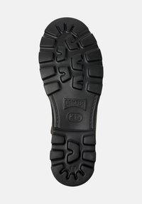 Semelle en caoutchouc noir avec des motifs de texture ; comprend des zones élevées pour l'adhérence et une section marquée "CAMPER" et la taille "42."