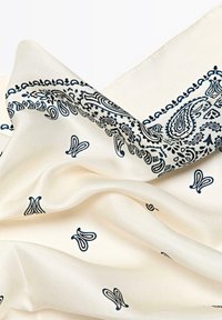 Écharpe en soie avec un fond crémeux orné de motifs paisley navy complexes et de délicates touches florales, affichant une texture lisse.