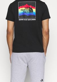 Black cotton t-shirt featuring a colorful mountain graphic and text on the back. Paired with gray sweatpants.