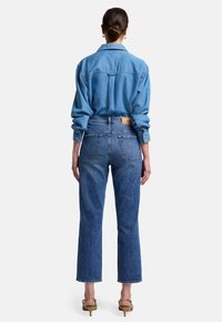 Chemise en denim bleu clair avec col, manches longues et poignets à bouton ; associée à un jean droit taille haute bleu avec poches arrière.