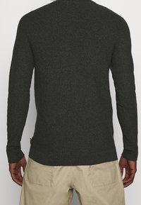 Pull en tricot vert foncé avec des manches longues, des poignets et un ourlet côtelés. Tissu texturé avec une finition lisse ; présente un petit accent sur le côté.