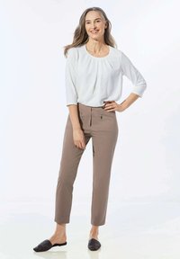 Witte geplooide blouse gecombineerd met tan tapering broek met ritszakken. Zwarte instapschoenen met textuurbewerkingen.