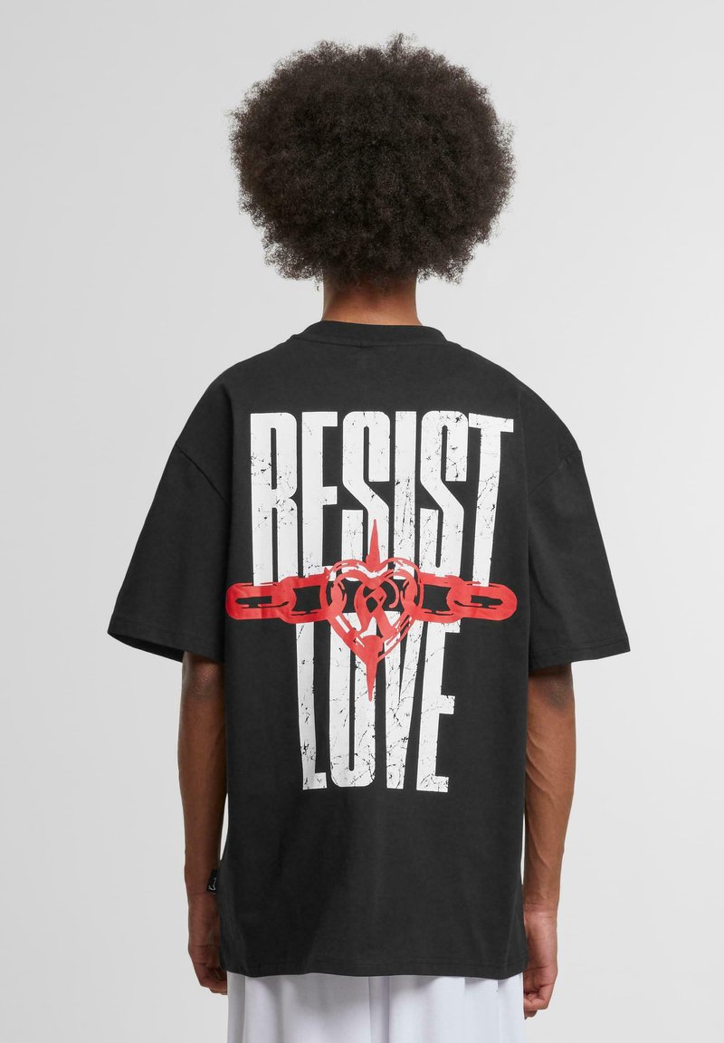 Black oversized t-shirt featuring bold white text "RESIST" and red heart and chain graphic design on the back. Cotton material, short sleeves.