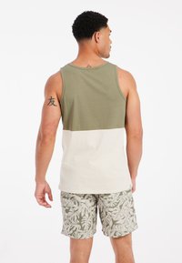 Canottiera verde oliva e bianca con design a blocchi di colore, realizzata in cotone. Abbinata a pantaloni corti con motivo foglia di palma in verde e beige.