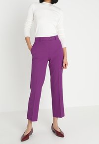 Lila skräddarsydda byxor med rak passform, framfickor, slät front och knäppning, kombinerat med en figursydd vit långärmad topp.