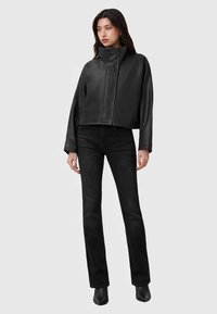 Μαύρο δερμάτινο κοντό μπουφάν με ψηλό γιακά, κλείσιμο με φερμουάρ μπροστά, σε συνδυασμό με μαύρο εφαρμοστό τζιν και μυτερά μαύρα μποτάκια αστραγάλου.