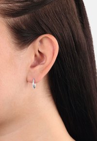 Orecchino a cerchio in argento con superficie liscia e lucidata, forma circolare e diametro ridotto, indossato nel lobo dell'orecchio.