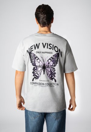 Graues T-Shirt mit großem lila Schmetterlingsmotiv auf der Rückseite, mit den Texten "NEW VISION ONLY HAPPINESS" und "COMPASSION COLLECTION".