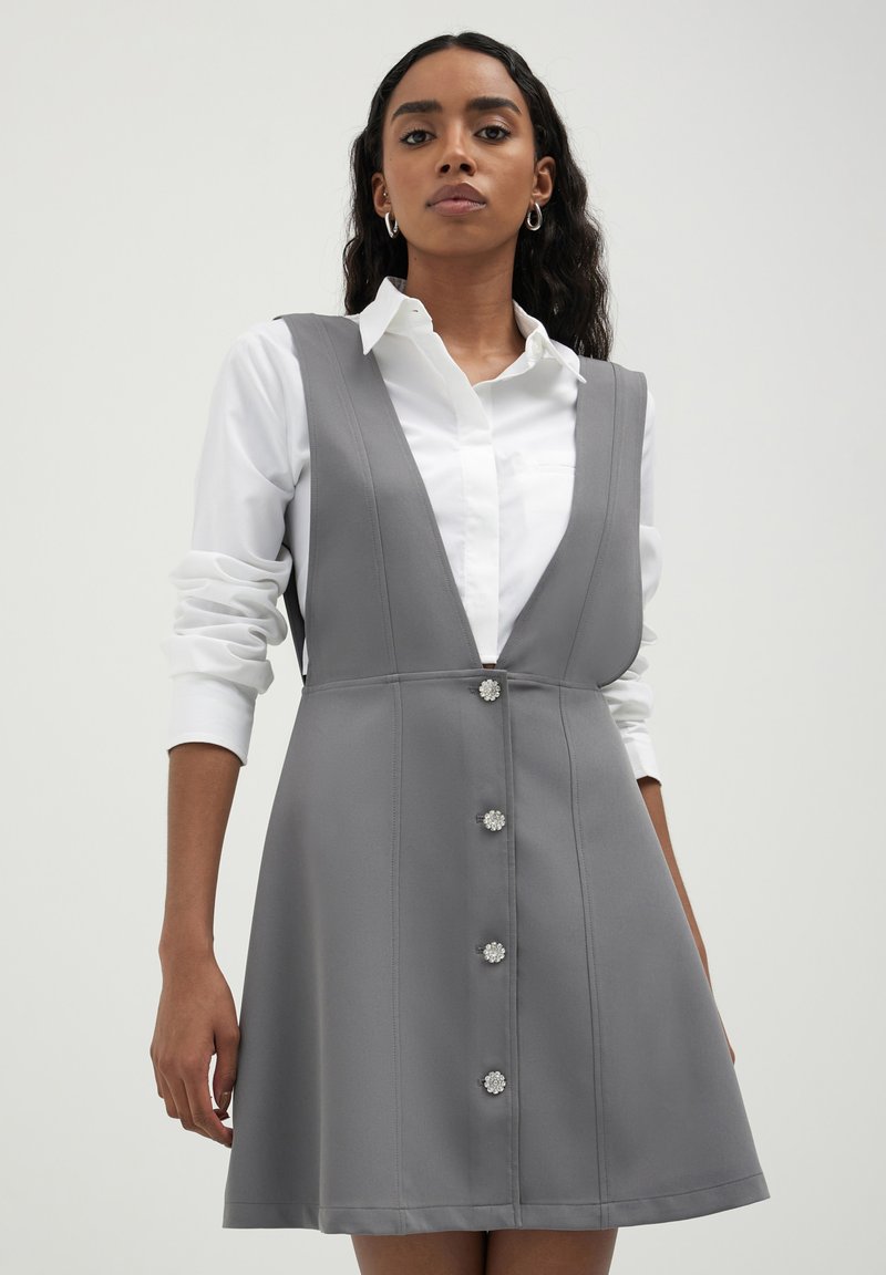 Robe grise en A avec un décolleté en V profond, sans manches, et six boutons fleuris sur le devant. Le tissu semble lisse et bien structuré.