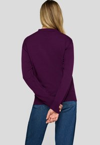 Lila Strickpullover mit langen Ärmeln, gerippten Bündchen und lässiger Passform, kombiniert mit blauen Jeans. Die Ansicht zeigt die Rückseite des Outfits.