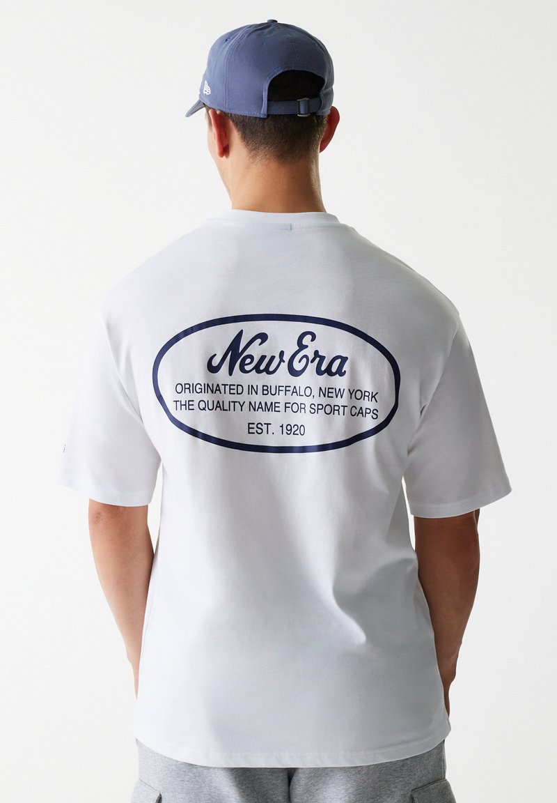 Bijela pamučna majica s okruglim, tamnoplavim logotipom na leđima, koja sadrži natpis "New Era" zajedno s informacijama o njenom porijeklu i godini osnivanja.