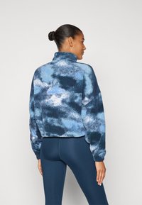 Fleece pullover with a high collar, featuring a blue and gray abstract pattern. Loose fit with dropped shoulders and ribbed cuffs.