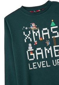 Jersey verde oscuro con arte de píxeles que muestra a Papá Noel, un muñeco de nieve, un reno, regalos, un árbol de Navidad y el texto "XMAS GAME LEVEL UP" en letras blancas de bloque.