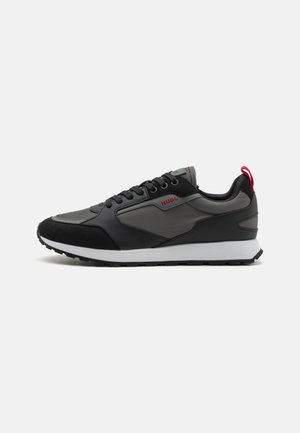 Sneakers noir et gris avec un mélange de cuir et de suède, dotés d'un système de laçage, d'une semelle intermédiaire blanche et d'un accent rouge à l'arrière.