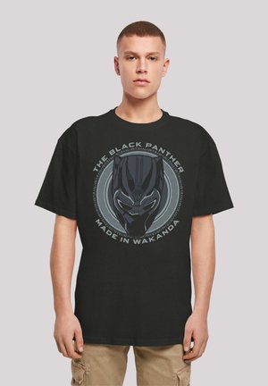 Svart bomull t-skjorte med et grafisk trykk av en Black Panther-maske med sirkulære stammønstre og teksten "MADE IN WAKANDA." Korte ermer.