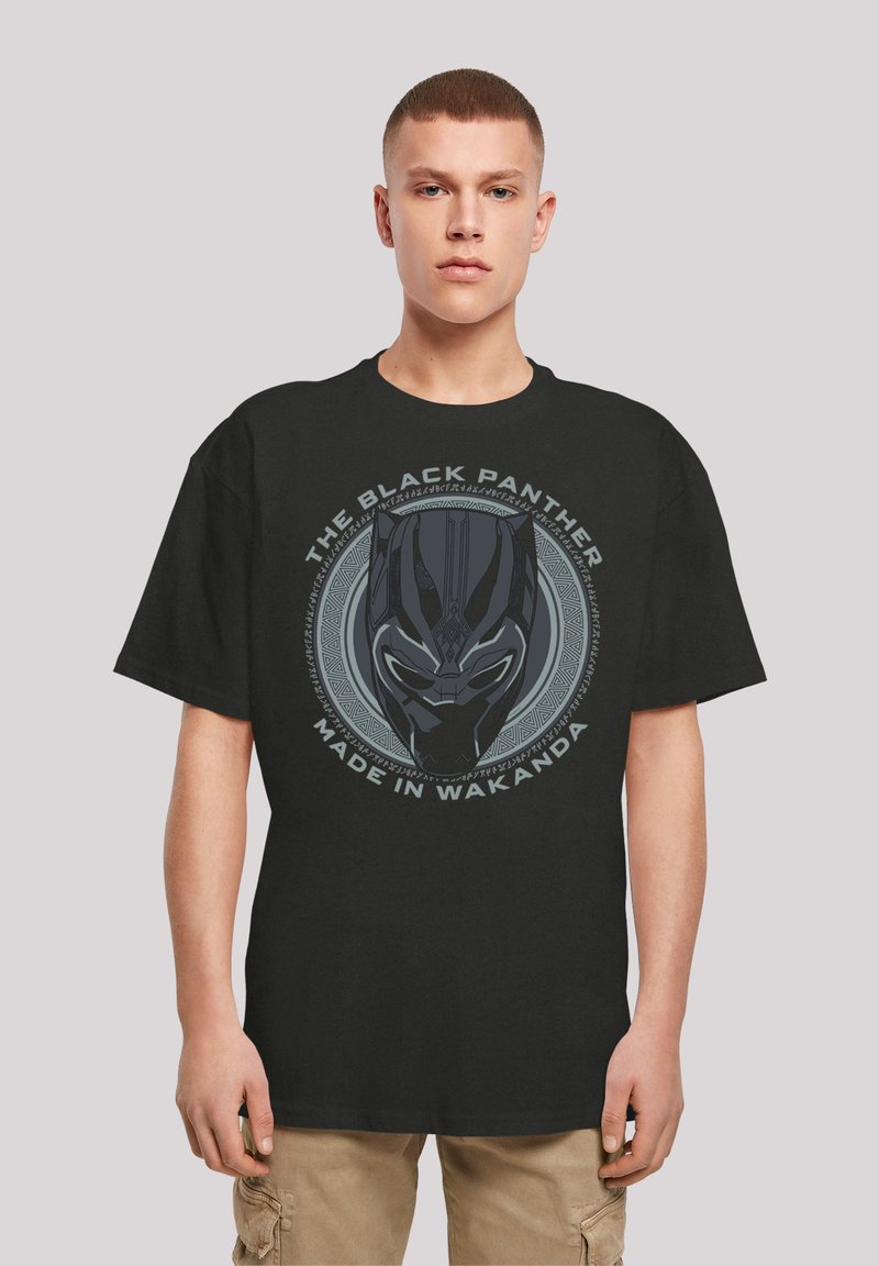 Svart bomull t-skjorte med et grafisk trykk av en Black Panther-maske med sirkulære stammønstre og teksten "MADE IN WAKANDA." Korte ermer.