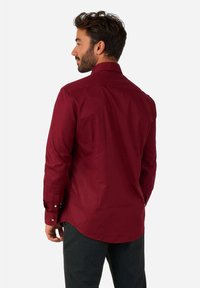 Camisa de manga larga burdeos con cuello clásico, puños abotonados y dobladillo curvado. Textura de tela suave sin patrones visibles.