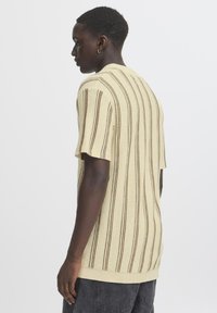 Strikket kortermet genser i lys beige med brune vertikale striper, med avslappet passform og ribbet kant. Strukturert stoff med et uformelt design.