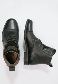 Stivali in pelle nera con punta rotonda, design con lacci e senza lacci, accenti laterali testurizzati e un tab in pelle marrone a contrasto sul tacco.