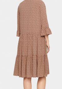 Robe à manches trois-quarts évasées en tissu doux de couleur pêche avec des pois noirs, présentant une jupe à volants et des détails de manches froncées.