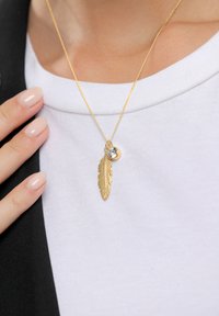 Goldkette mit einem Federanhänger und einem kleinen, runden, klaren Edelstein. Die Kette ist fein und zierlich und ergänzt das metallische Finish.