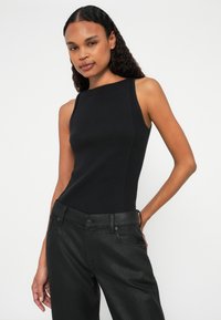 Top in maglia nera a costine con un design aderente, caratterizzato da un collo alto e senza maniche, abbinato a pantaloni neri texturizzati.