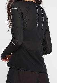 Camiseta atlética negra de manga larga con paneles de malla y acentos reflectantes. La tela es ligera y tiene un diseño ajustado.