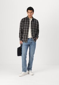 Black and white checkered button-up shirt, white t-shirt underneath, light blue jeans, and white sneakers, holding a black bag.