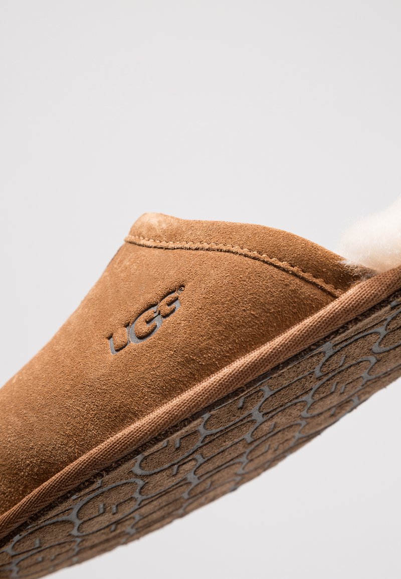 Braune Wildlederslipper mit einem weichen Innenfutter, verziert mit einer gesteppten Kante und einer strukturierten Gummisohle mit Logodetail.
