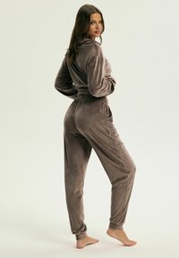 Zestaw dresowy z weluru w kolorze taupe, z kapturem oraz dopasowanymi spodniami z elastycznym pasem i mankietami, charakteryzujący się miękką fakturą.