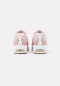 Nike-sneakers har en mjuk rosa ovandel med läder- och mesh-texturer, vita gummisulor och transparent luftdämpning vid hälen.