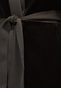 Czarna aksamitna tkanina z satynową ciemnoszaro wstążką zawiązaną w węzeł. Materiał ma miękką strukturę, podkreślając luksus i wyrafinowanie.