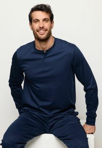 Setti loungewear tummansinisestä väristä, joka sisältää pitkähihainen henley-paita, jossa on kaksi nappia ja pehmeä kangas, sekä yhteensopivat housut, joissa on joustava vyötärö.