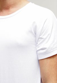 Camiseta blanca de algodón con cuello redondo y mangas enrolladas, textura suave, diseño ajustado y sin patrones ni acentos visibles.