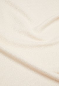 Tekstūruota kreminės spalvos medžiaga su minkštu, austu raštu, rodanti subtilius atspalvių skirtumus ir lygią paviršių, tinkama įvairioms paskirtims.