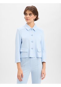 Lichtblauwe cropped jas met een puntige kraag, vijf knopen aan de voorkant en twee opgestikte zakken. Soepele textuur met gestructureerde naden.